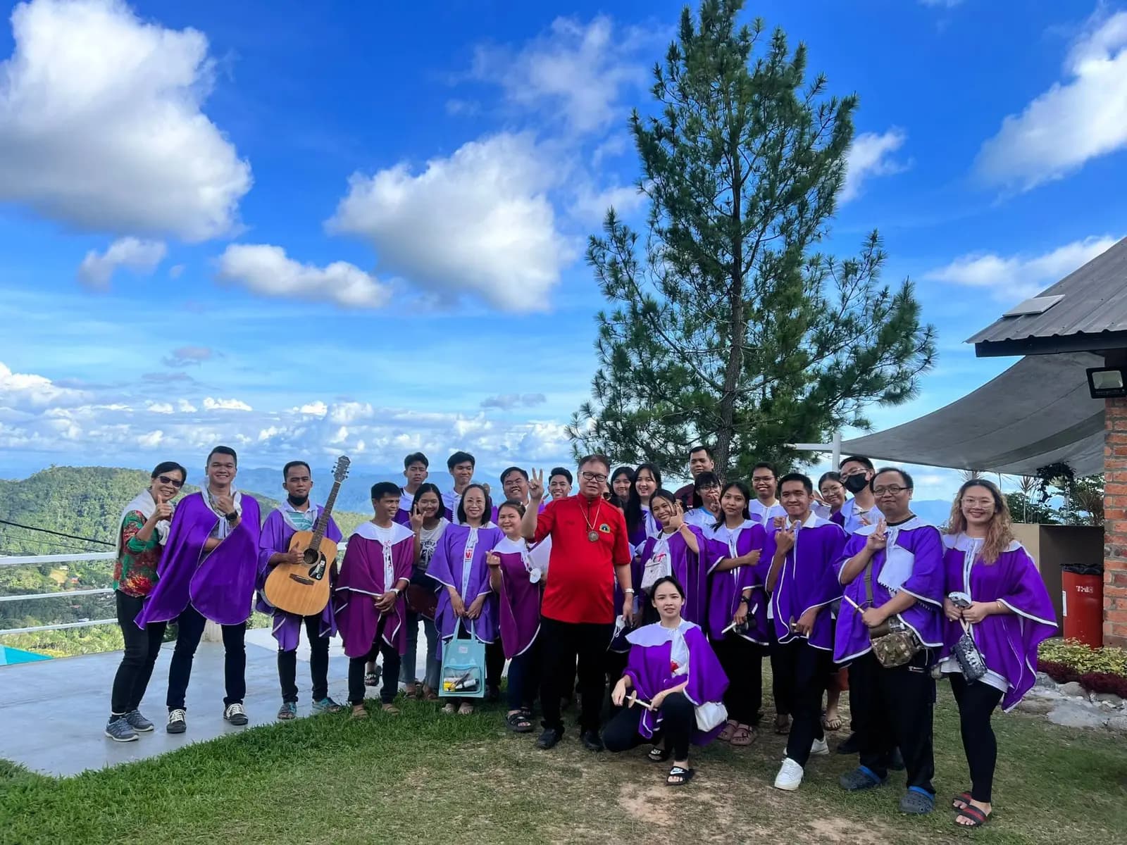 A church choir in purple robes on the lawn at The Hill Kinabalu with hills and blue sky behind