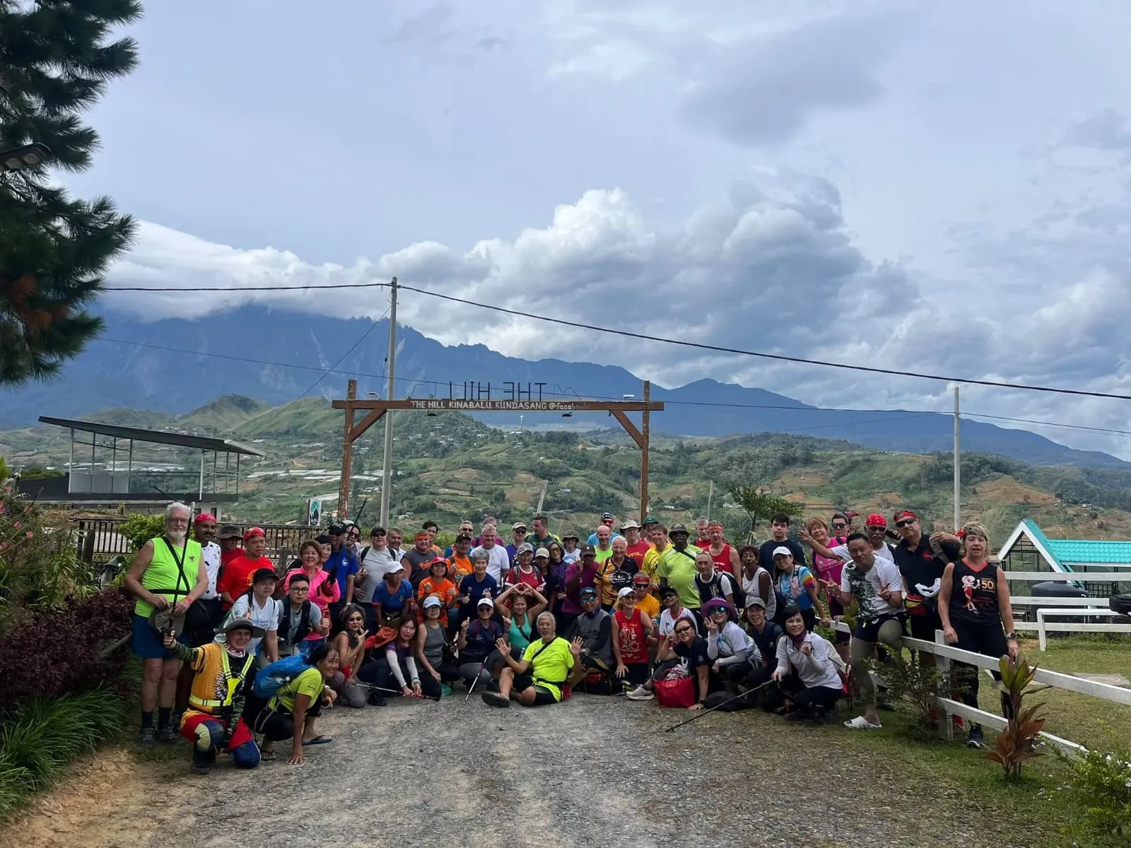 A large hiking group posing at The Hill Kinabalu gate with Mount Kinabalu in the background