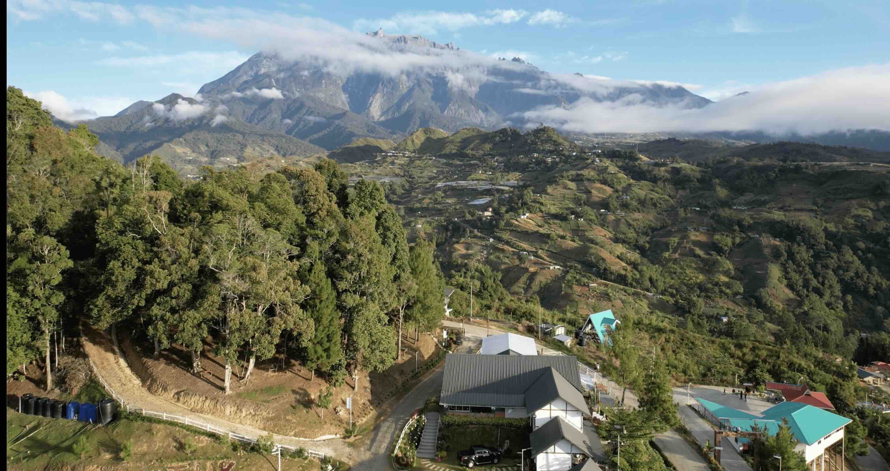 An aerial view of The Hill Kinabalu with Mount Kinabalu rising beyond the green hills